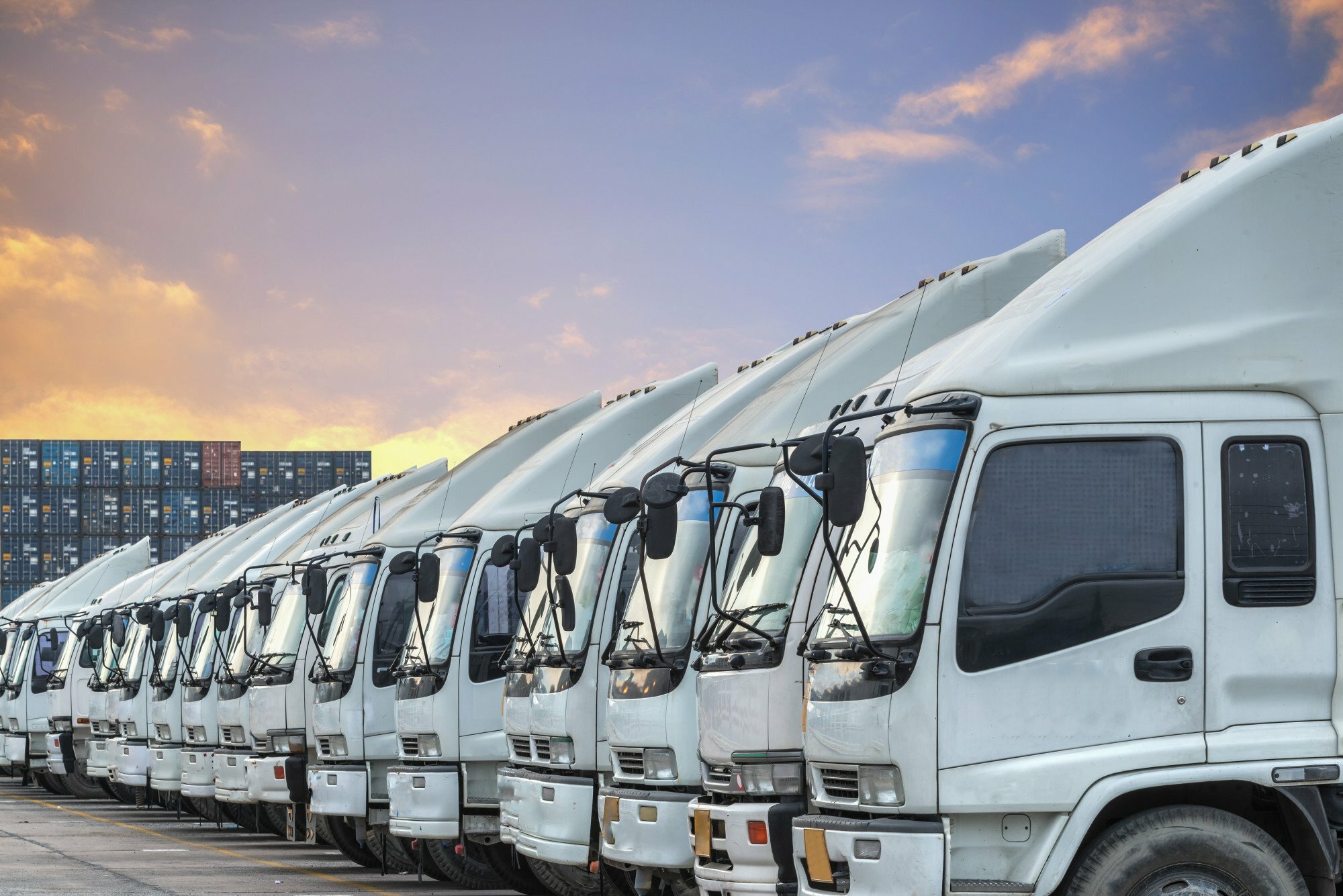 Row of white delivery trucks parked in a fleet yard at sunset.